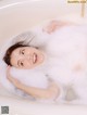 A woman laying in a bathtub with foam on her face.