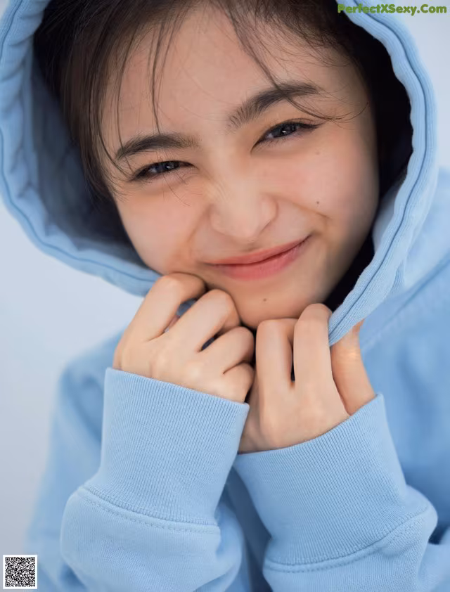 A young girl in a blue hoodie smiles at the camera.