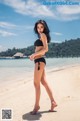 A woman in a black bikini standing on a beach.