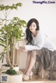 A woman sitting on a chair next to a potted plant.