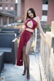 A woman in a red dress posing on a balcony.