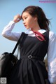 A woman in a black dress and white shirt holding a black bag.