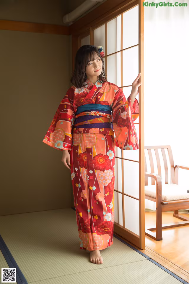 A woman in a red kimono standing in front of a window.