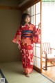 A woman in a red kimono standing in front of a window.