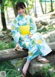 A woman in a blue and yellow kimono sitting on a log.