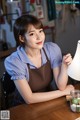 A woman in an apron sitting at a table with a lamp.