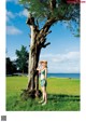 A woman standing next to a tree in a grassy field.