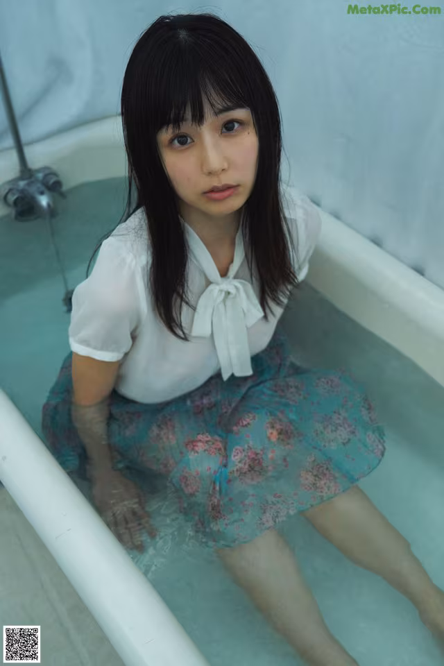 A woman sitting in a bathtub with her legs in the water.